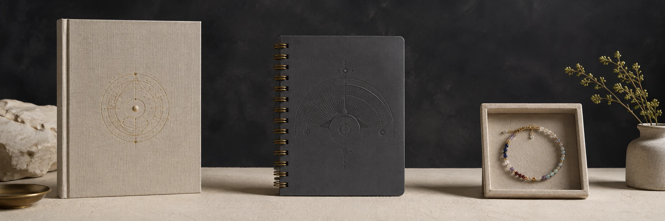 A linen birth book, six-month planner, and gemstone bracelet in a warm studio setting